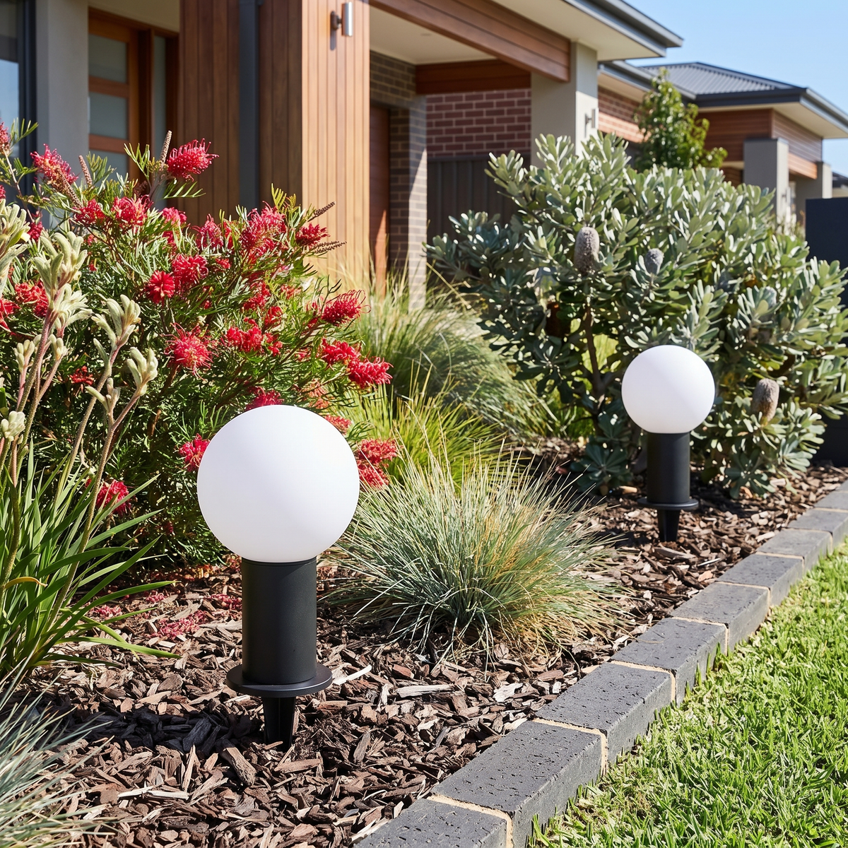 Two Allen LED bollard lights on ground spikes in a native grevillea garden bed on a bright day