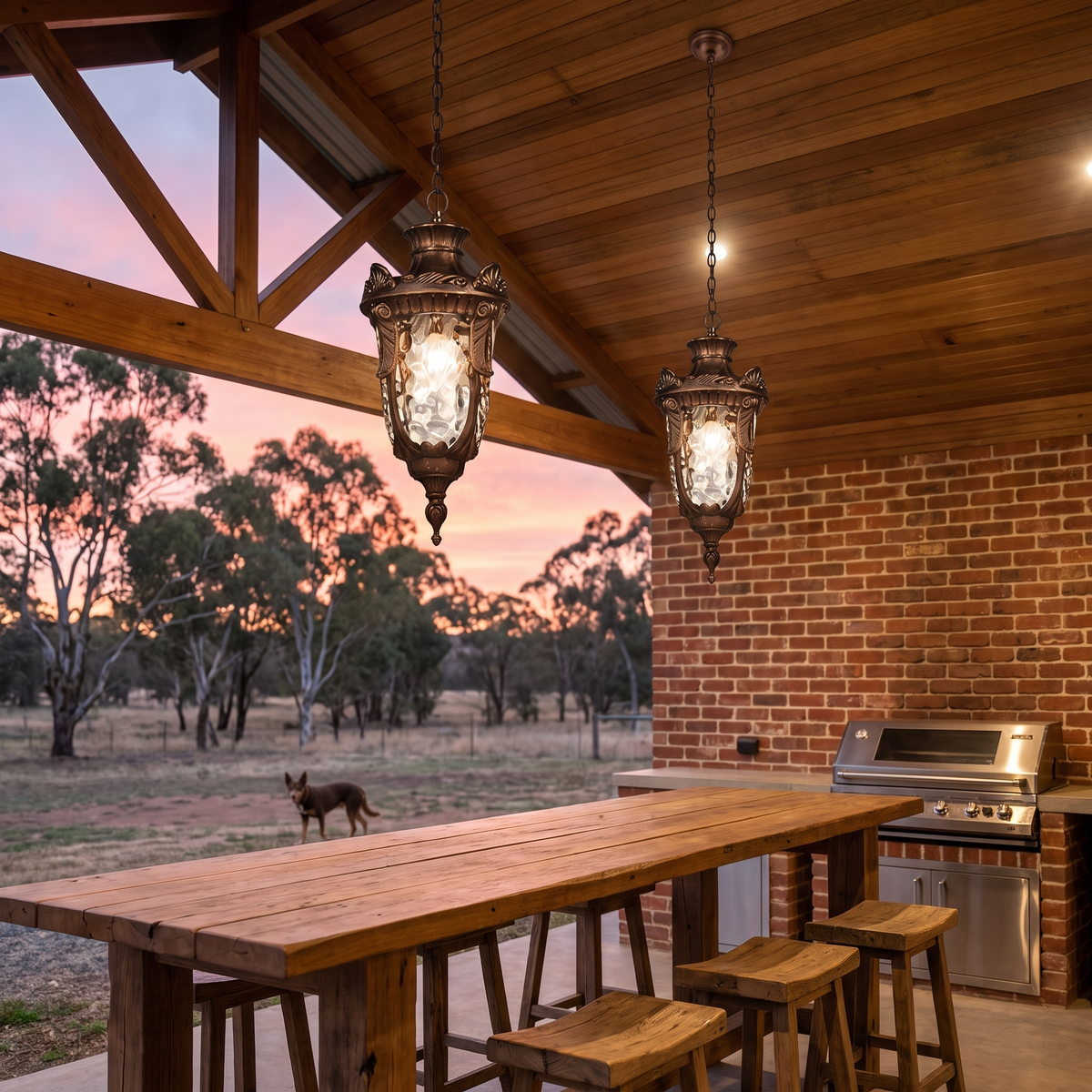 Two Anita bronze lantern pendants over a timber bar in a covered farmhouse outdoor kitchen at dusk