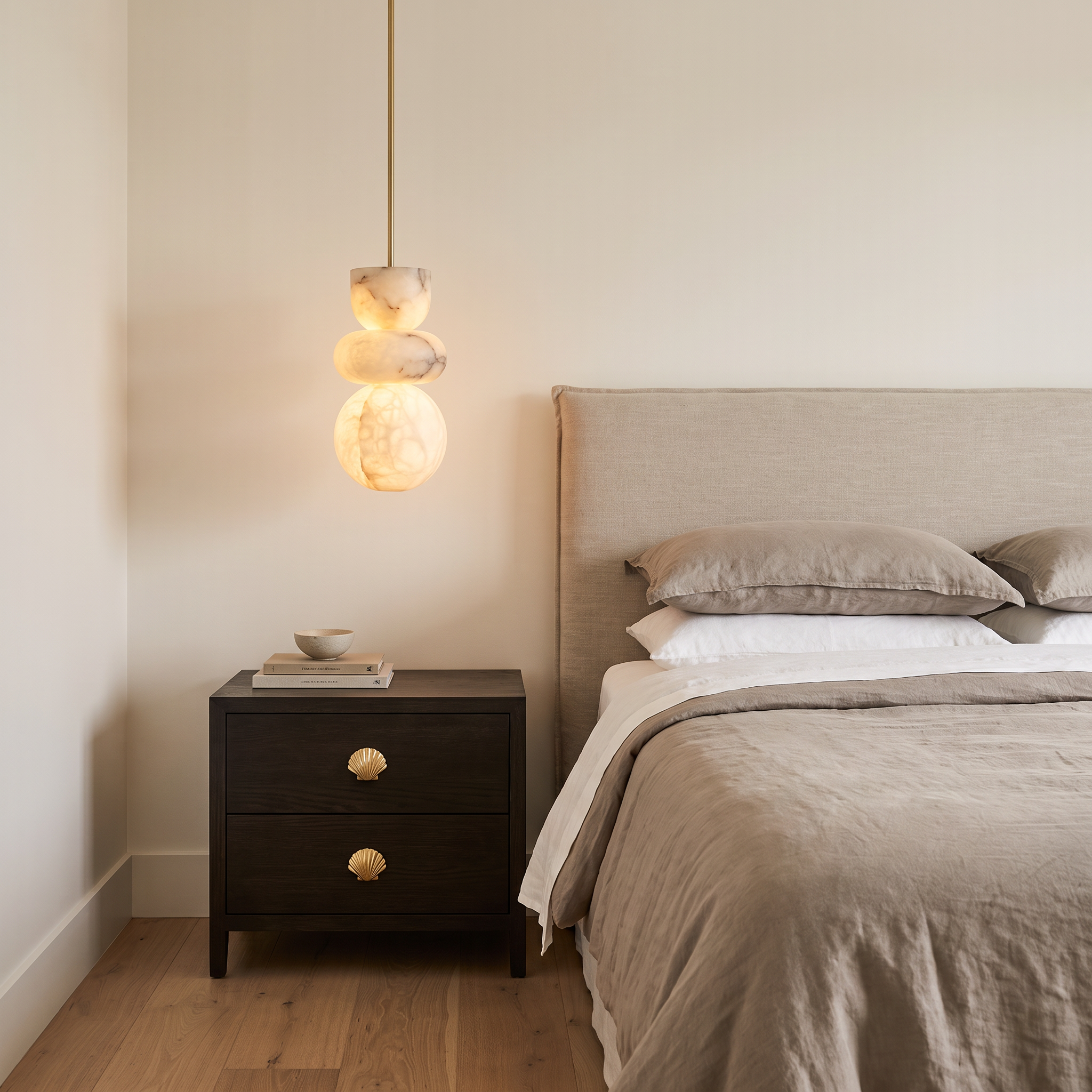 Aquila alabaster pendant light beside a bed above a dark timber bedside table with brass shell handles in a styled bedroom