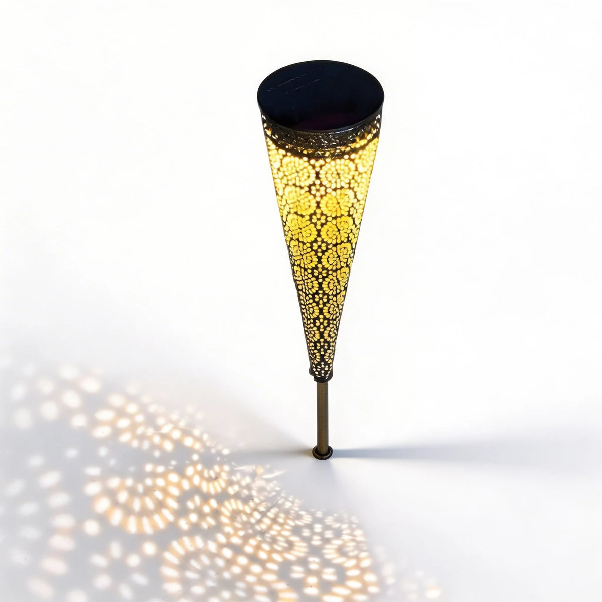 Bili Solar Garden Light glowing warm through its black lace metal cone, casting a dappled pattern on the ground