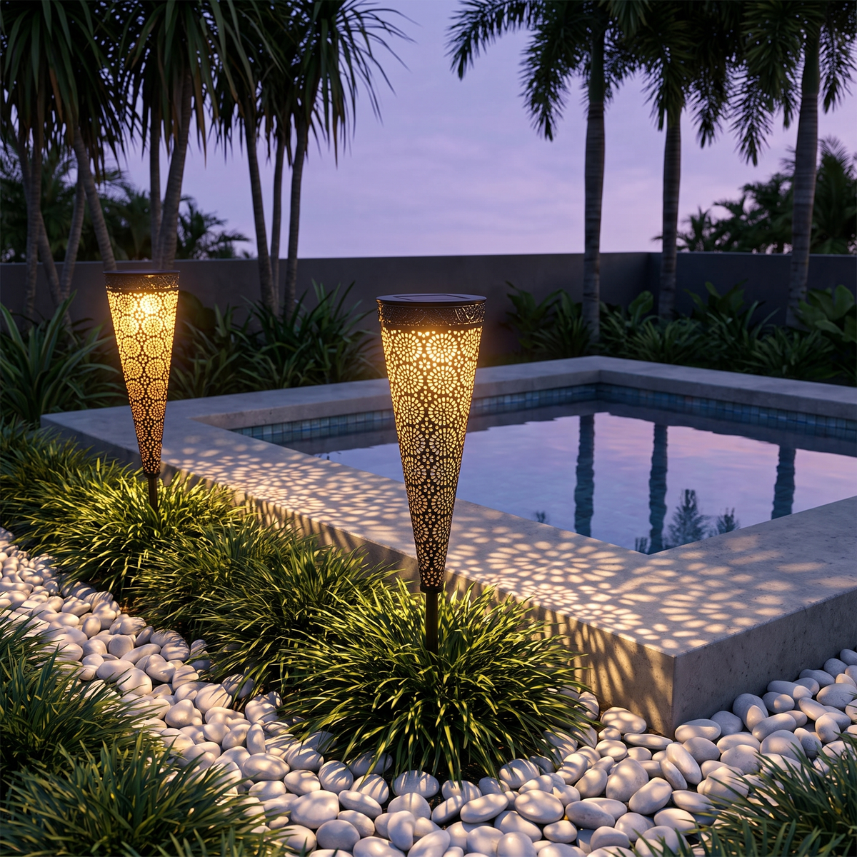 Two Bili Solar Garden Lights glowing in a white pebble bed by a plunge pool with bangalow palms at dusk