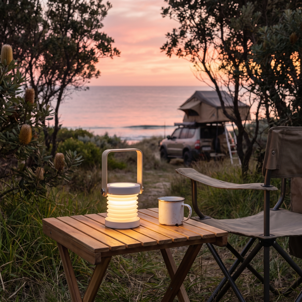 Brae rechargeable travel lantern in grey on a camp table at a beach campsite beside a 4WD at dusk
