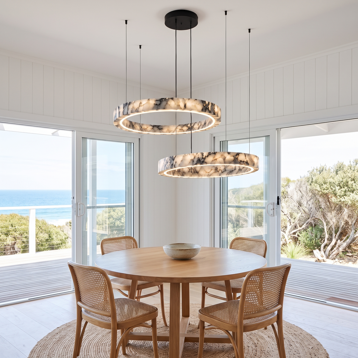 Byron two-ring marble chandelier hanging over a round oak dining table in a coastal beach house