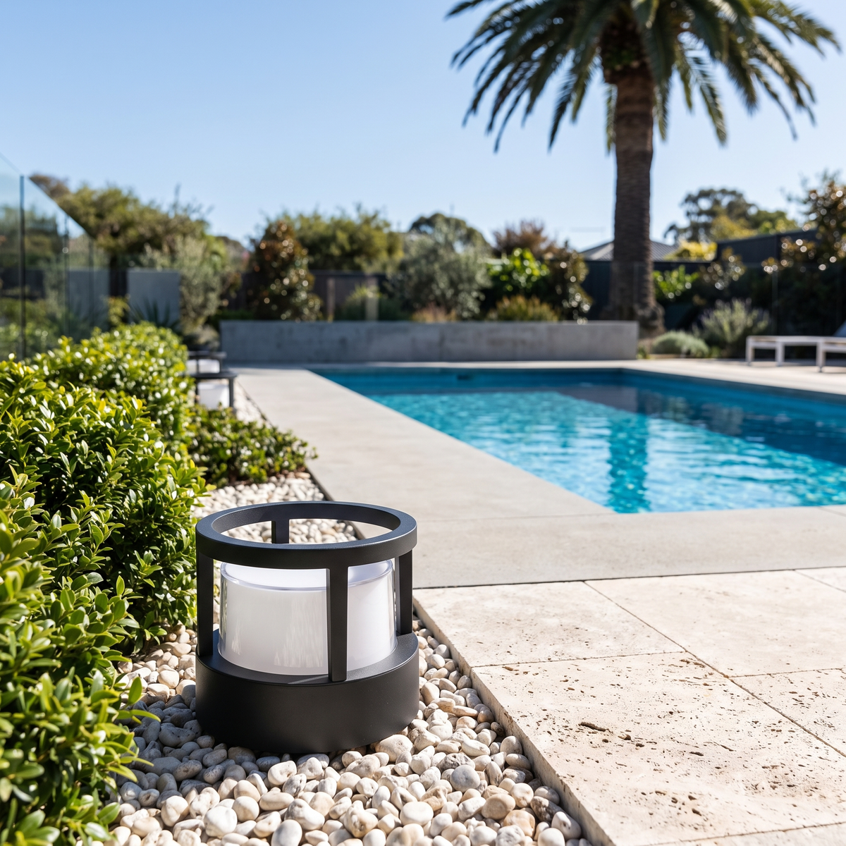 Cally LED garden post light with hollow crown in a pebble strip beside a travertine lap pool