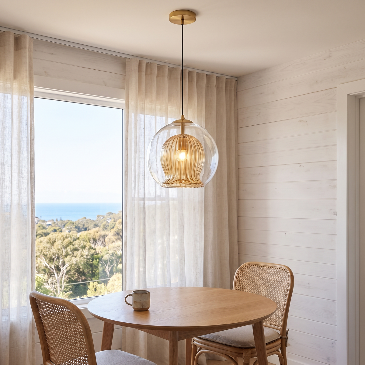 Capri amber glass pendant above a round oak table in a coastal breakfast nook with ocean views