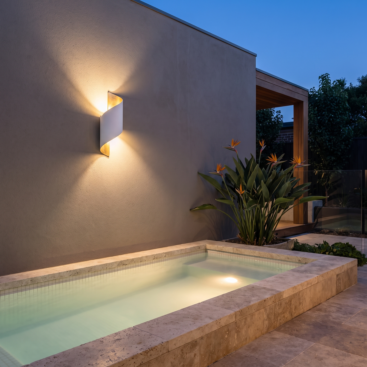 Clarry Outdoor Wall Light in white and gold in a rendered courtyard by a plunge pool at dusk