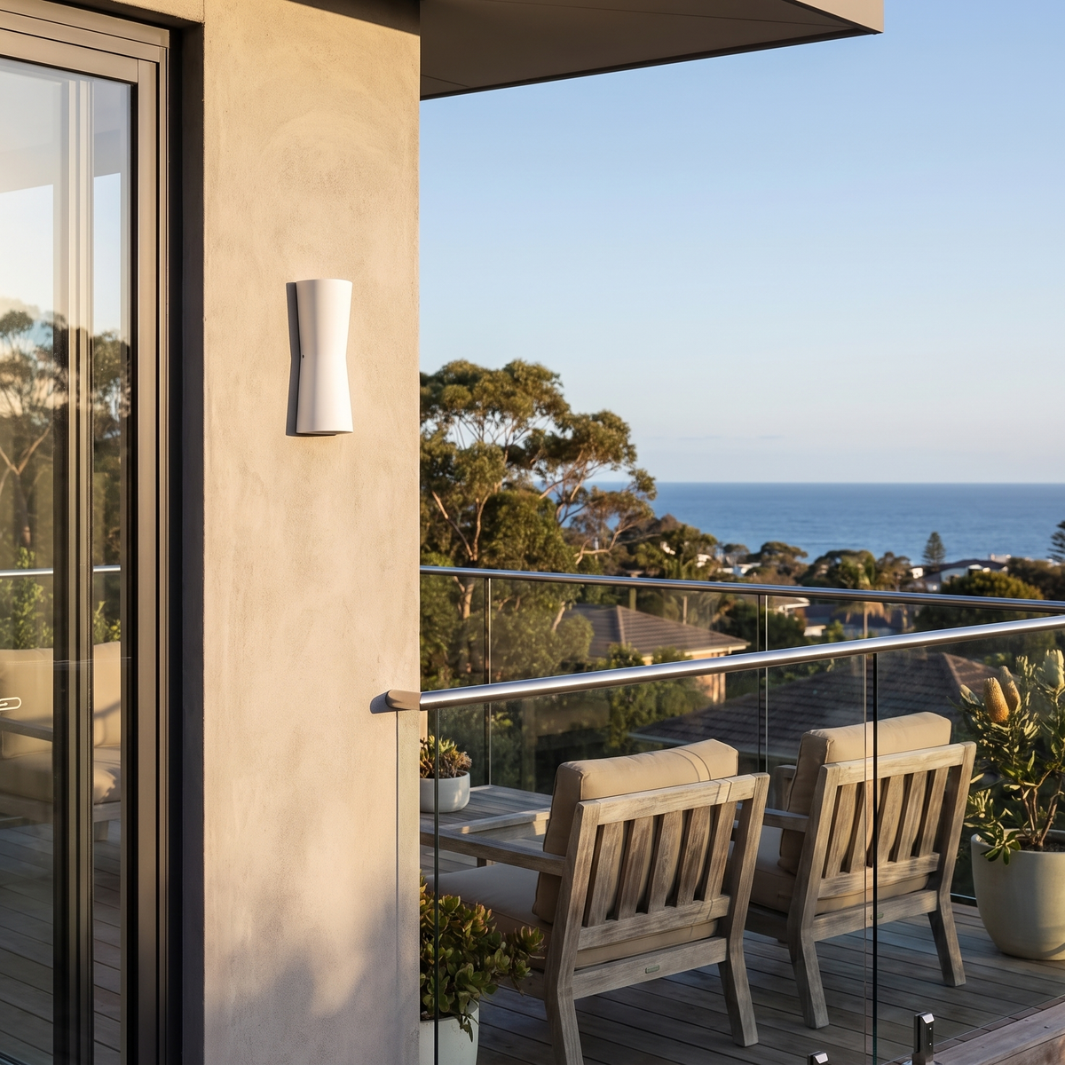 Dewy torch-style outdoor wall light in white on a concrete balcony wall with an ocean view