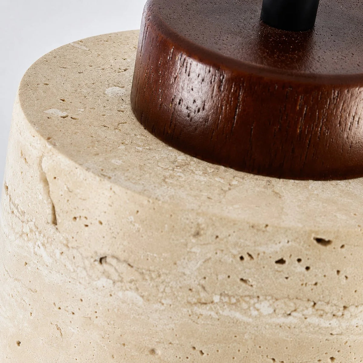 Close-up of the Dural pendant's walnut cap sitting on the pitted natural travertine shade