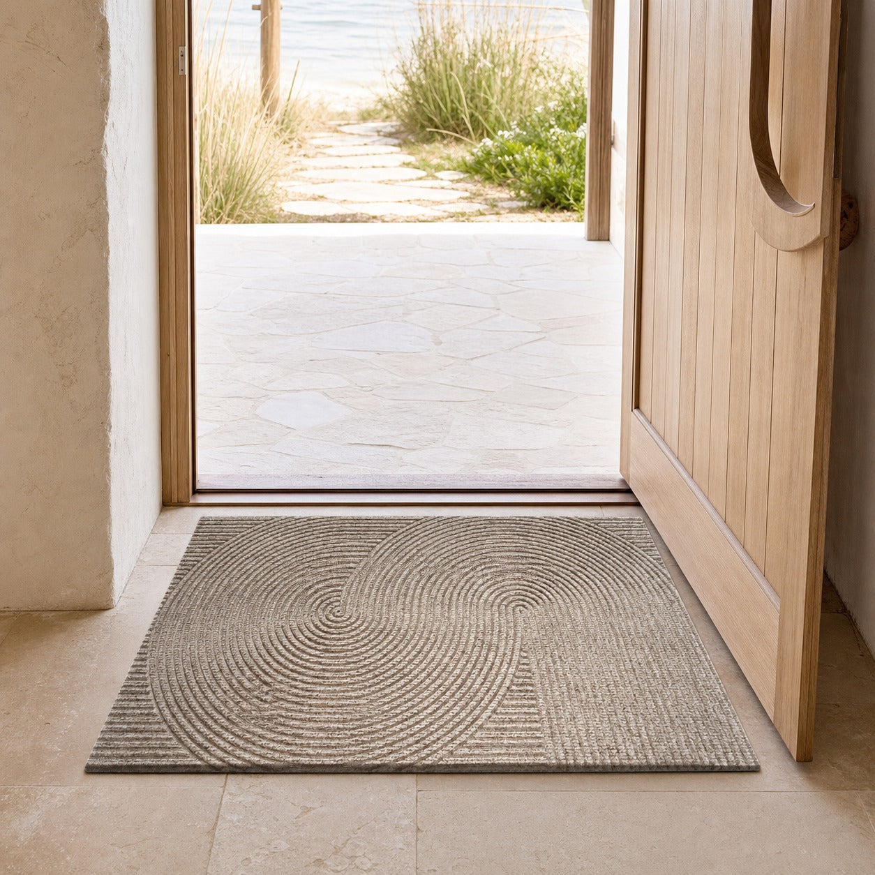 A rectangular entryway doormat with a textured circular ripple pattern in shades of beige and gray, shown on a tiled floor leading to an open wooden door and outdoor patio.