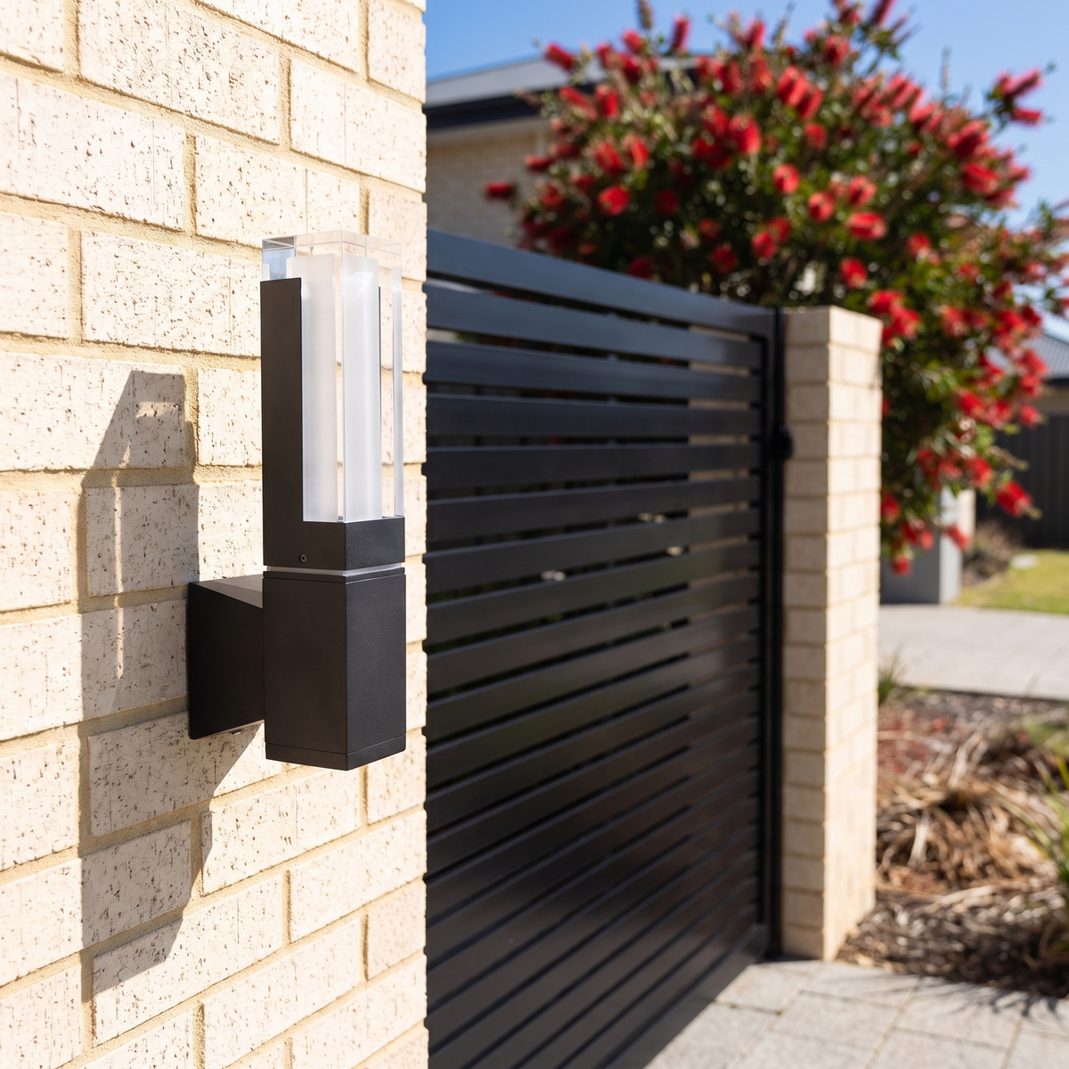 Freo Outdoor Wall Light, 7W, on cream brick beside a black slatted driveway gate on a sunny day