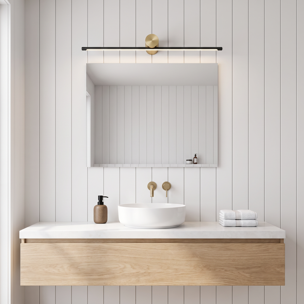 Black and gold Hartog vanity light bar above a mirror with an Eron soap dispenser and Terry striped towels
