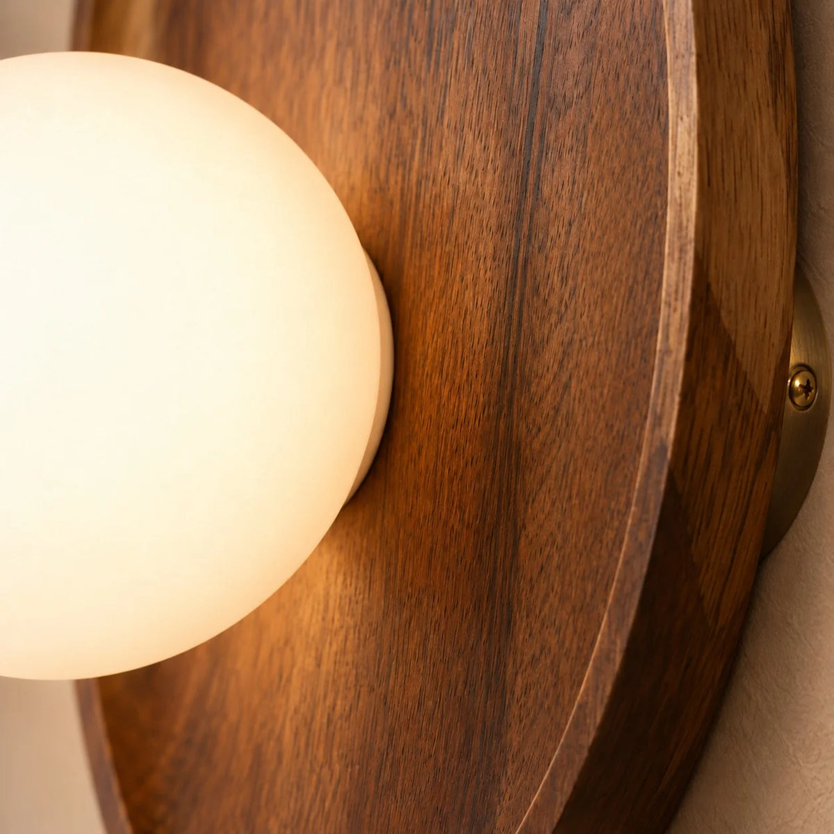 Detail of the Henny walnut backplate bevelled rim beside its glowing opal glass globe