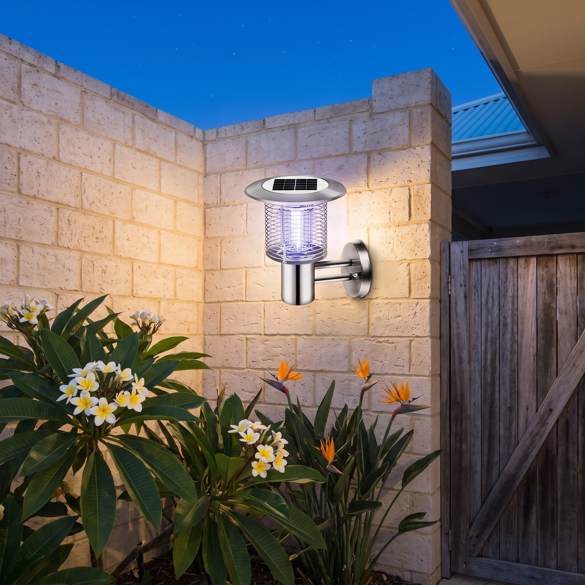 Juli Solar Bug Zapper Light in silver mounted on a brick courtyard wall by a timber gate with frangipani at dusk