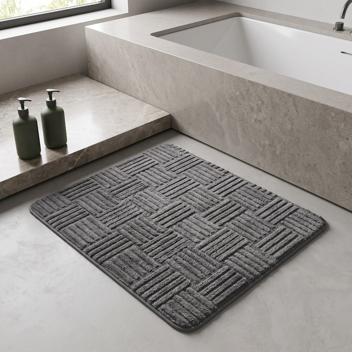 Marden striped non-slip bath mat in dark grey on a marble floor beside a built-in bath
