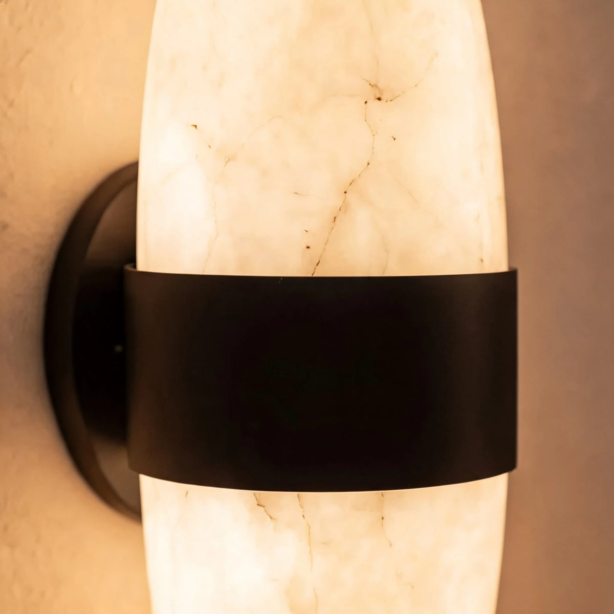 Detail of the Nula black stainless steel band and wall mount across glowing alabaster