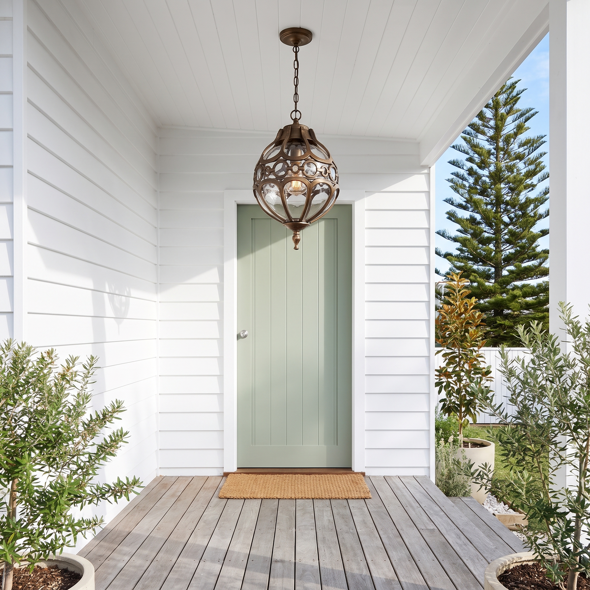 Olly glass globe outdoor pendant in bronze on a covered beach house porch by a sage door in the morning