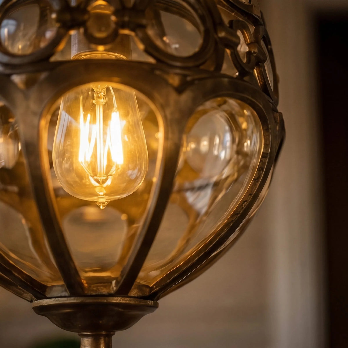 Close-up of the Olly pendant's bronze cage and clear glass lenses around a glowing filament bulb