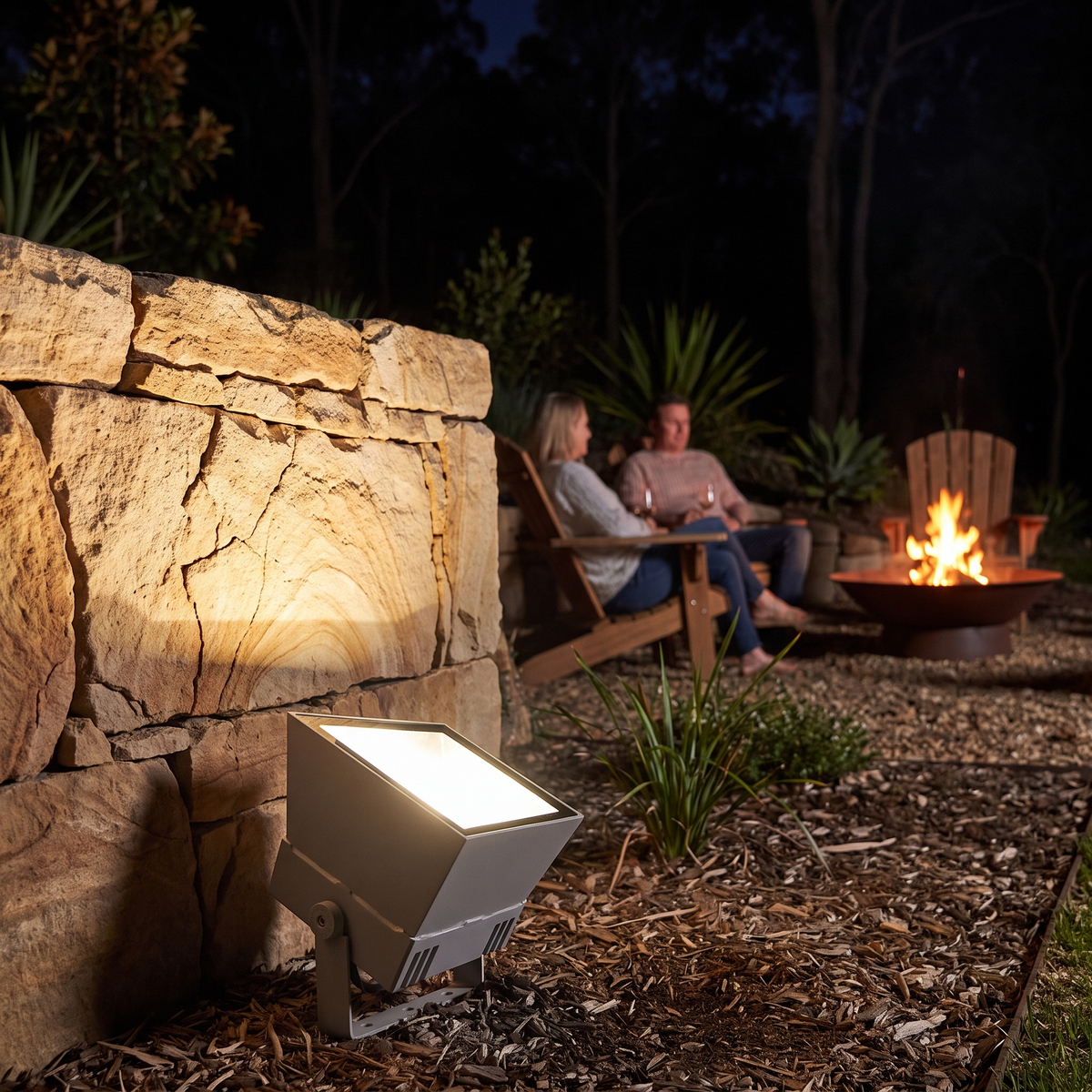 Oxford RGB outdoor spotlight grazing a sandstone feature wall beside a fire pit at night