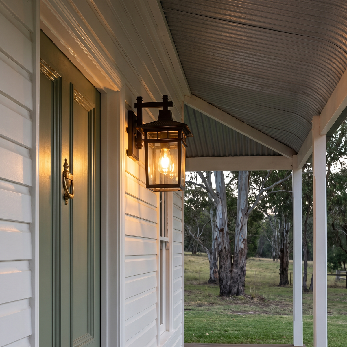 Pica Retro Outdoor Wall Lantern in black on a white weatherboard farmhouse verandah at dusk