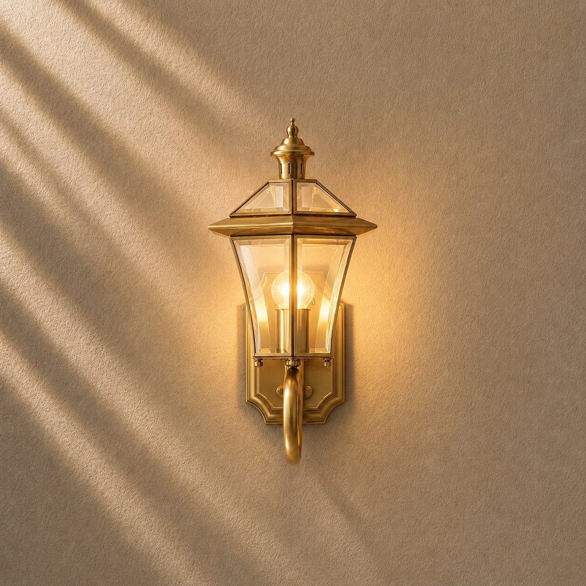 Sade outdoor wall lantern in brass with clear glass panels on a scrolled wall bracket