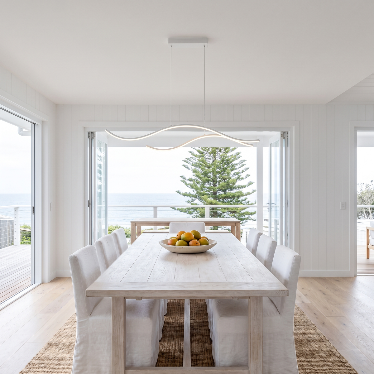 Soho white 100cm wave LED pendant above a beach house dining table