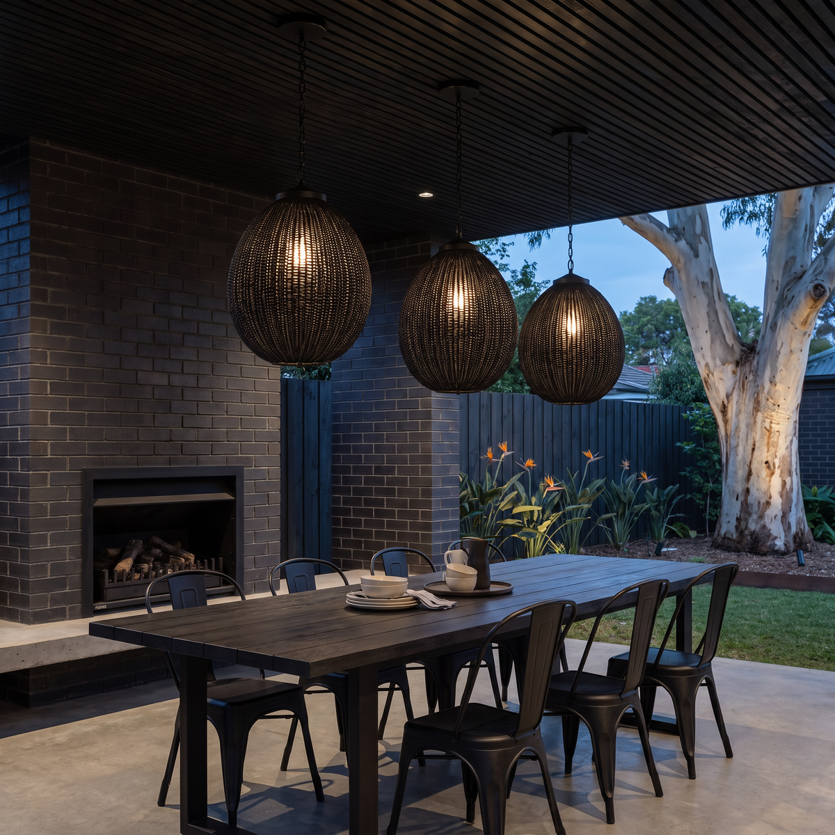 Three egg-shaped Suka woven outdoor pendants glowing over a dark table in a covered pavilion at night