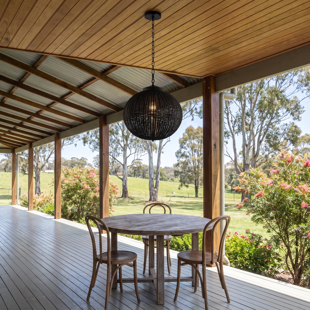 Round Suka black rattan pendant light over a timber table on a hinterland homestead verandah in the morning