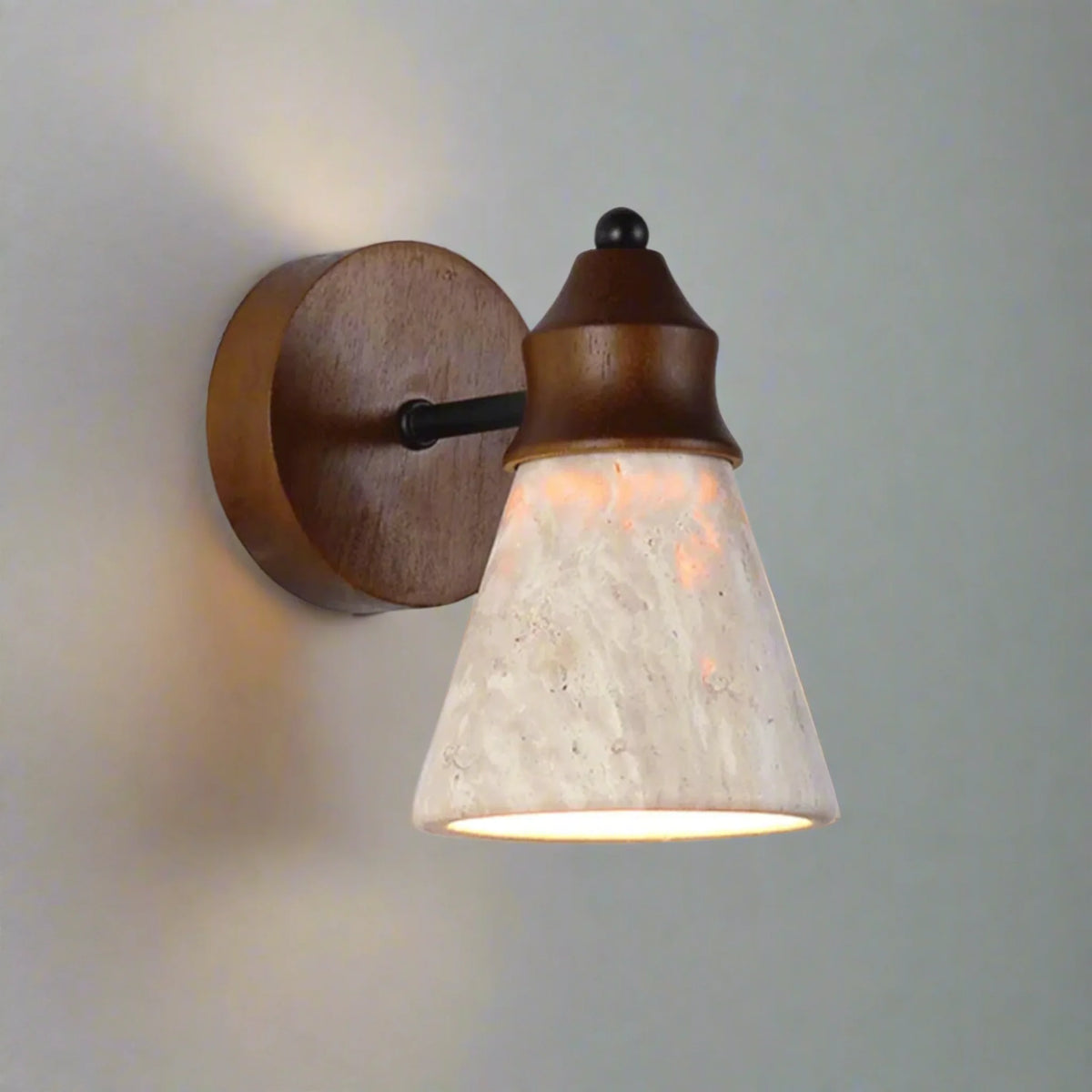Telo travertine wall sconce with a dark timber plate and cap and a lit travertine cone shade