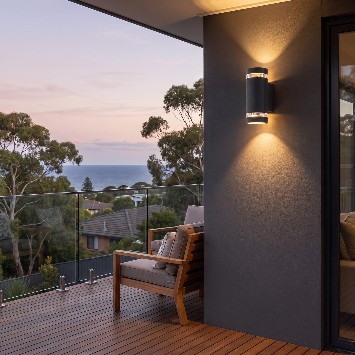 Visage up down wall light on a charcoal balcony wall with glass balustrade and ocean view at dusk