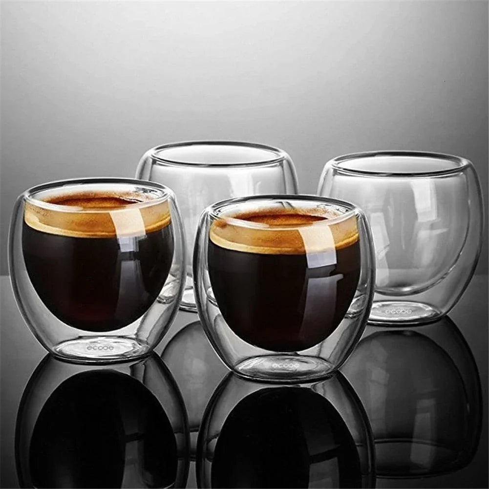 Four Zorin double-wall glass espresso cups, two filled with espresso, on a reflective grey surface